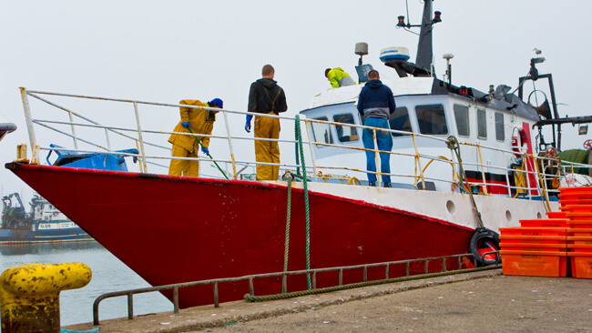 red fishing trawler berthed at pier with three fishermen on board